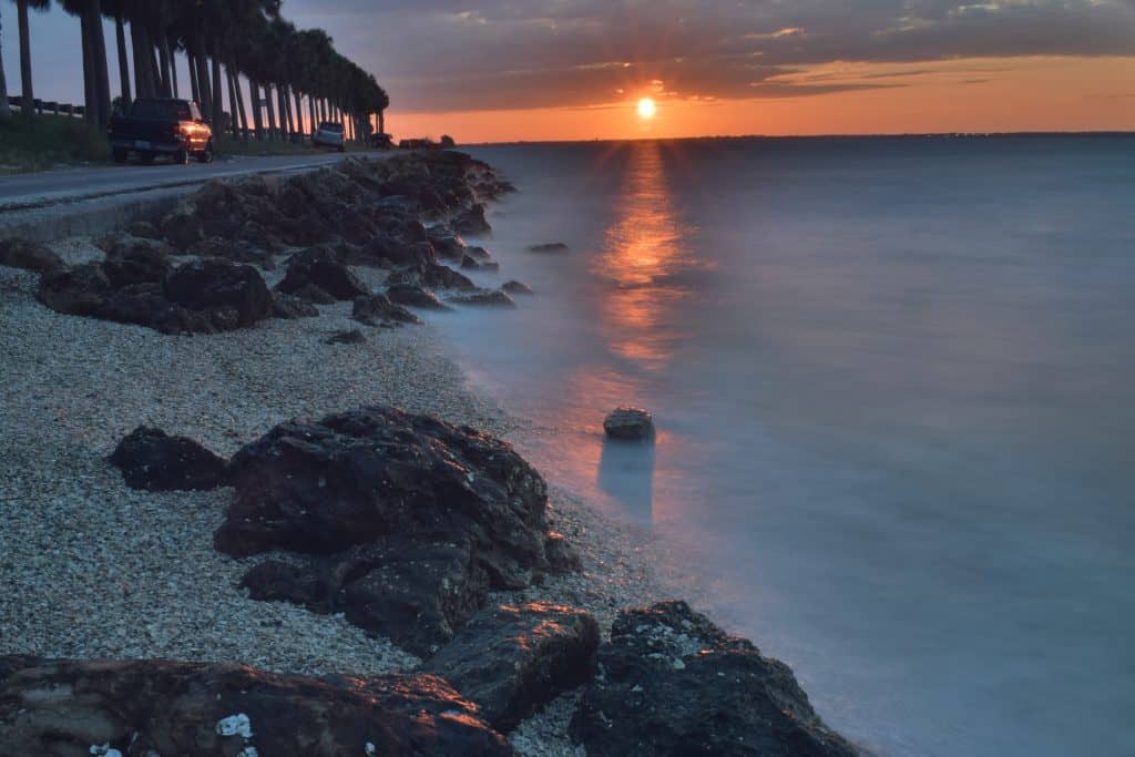 The waves lap at the rocky beach and trail along the Courtney Campbell Causeway Beach at sunset.