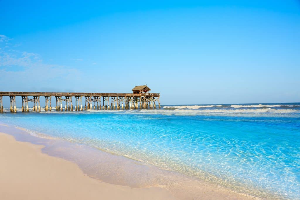 The crystal clear, blue waters lap at the shores of Cocoa Beach with the pier in the background.