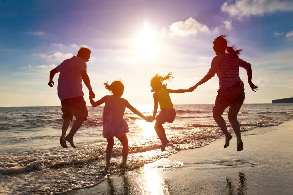 A silhouetted family jumps as the waves crash on the shoreline underneath their feet.