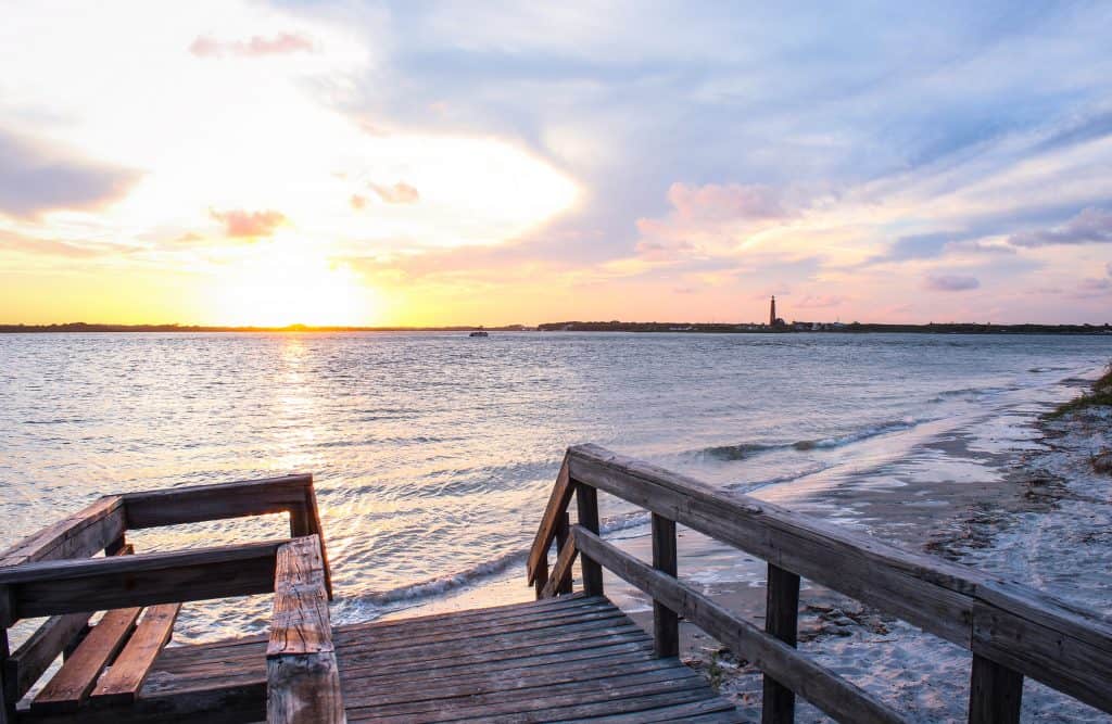 A boardwalk steps down to the sandy shores of New Smyrna Beach at sunset.