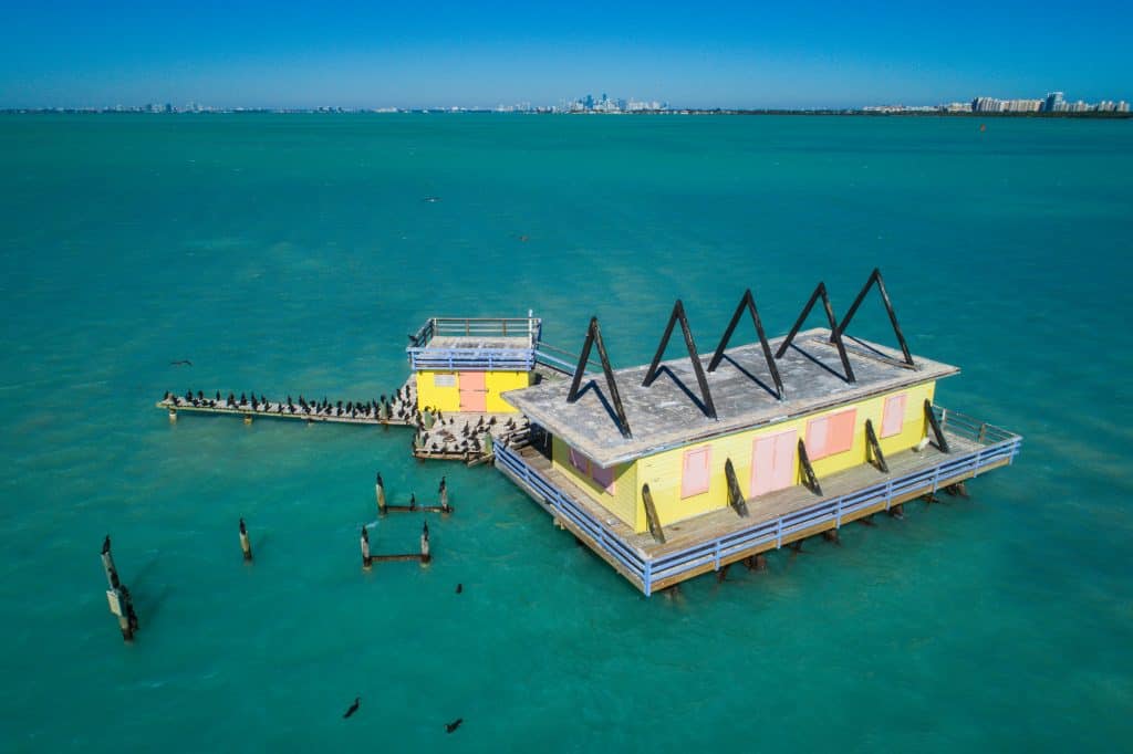 A colorful home hovering over the green waters in Stitlsville is covered in birds in Biscayne Bay, one of the best things to do in Miami.