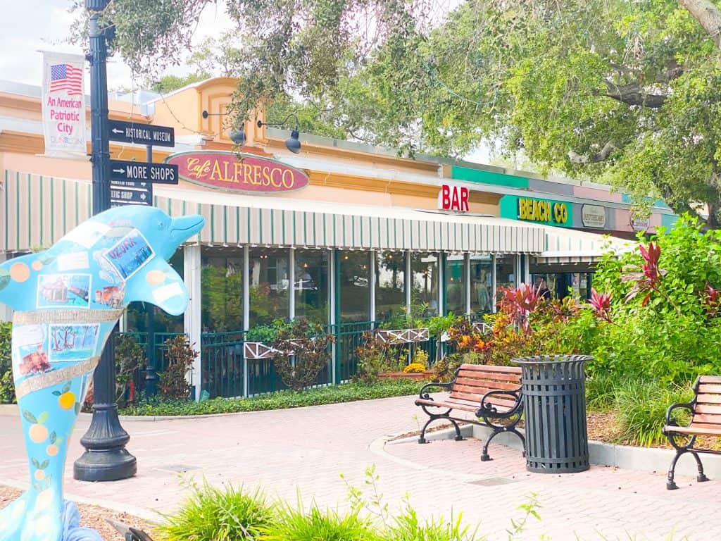 A brick walkway, benches, and a Florida dolphin sit outside the garden patio of Cafe Alfresco.