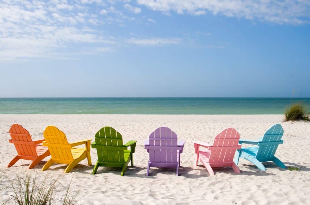 Colorful chairs are arranged on the sand to face the shoreline of Captiva Beach.