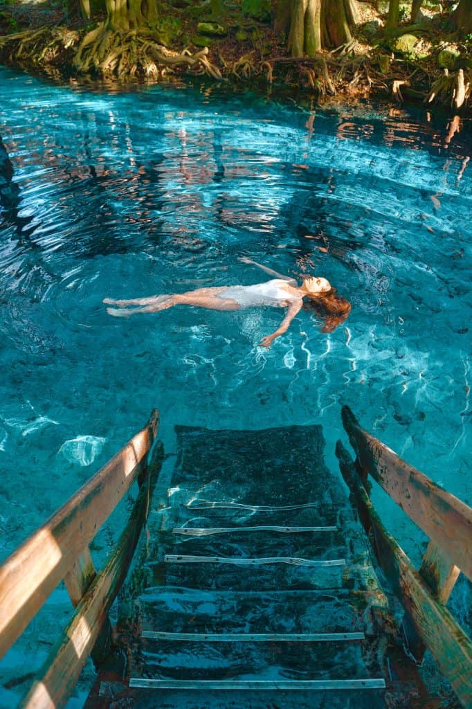 A woman in a white swim suit floats in the waters of Ginnie Springs, her hair undulating underneath her.