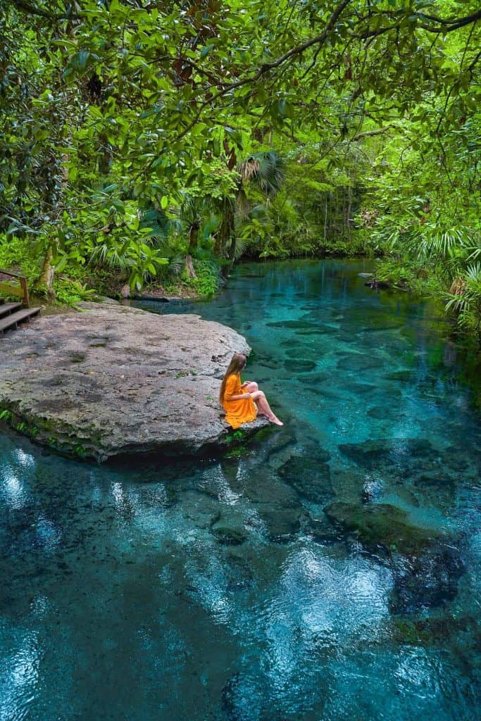 A woman in a yellow dress sits on the edge of the water at Rock Springs one of the best Tampa springs.