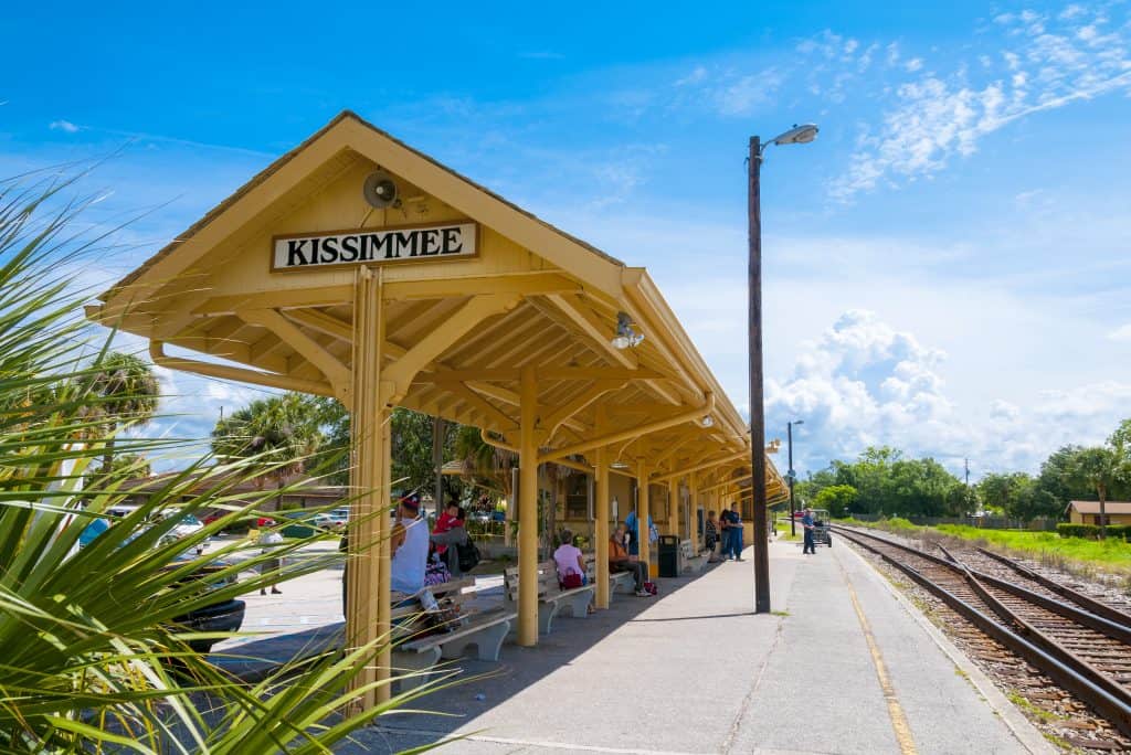 A train depot sits in the city, marked with the town's name, as guests wait.