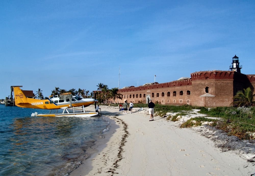 People disembarking the seaplane at the beach at Dry Tortugas National Park with Fort Jefferson nearby.