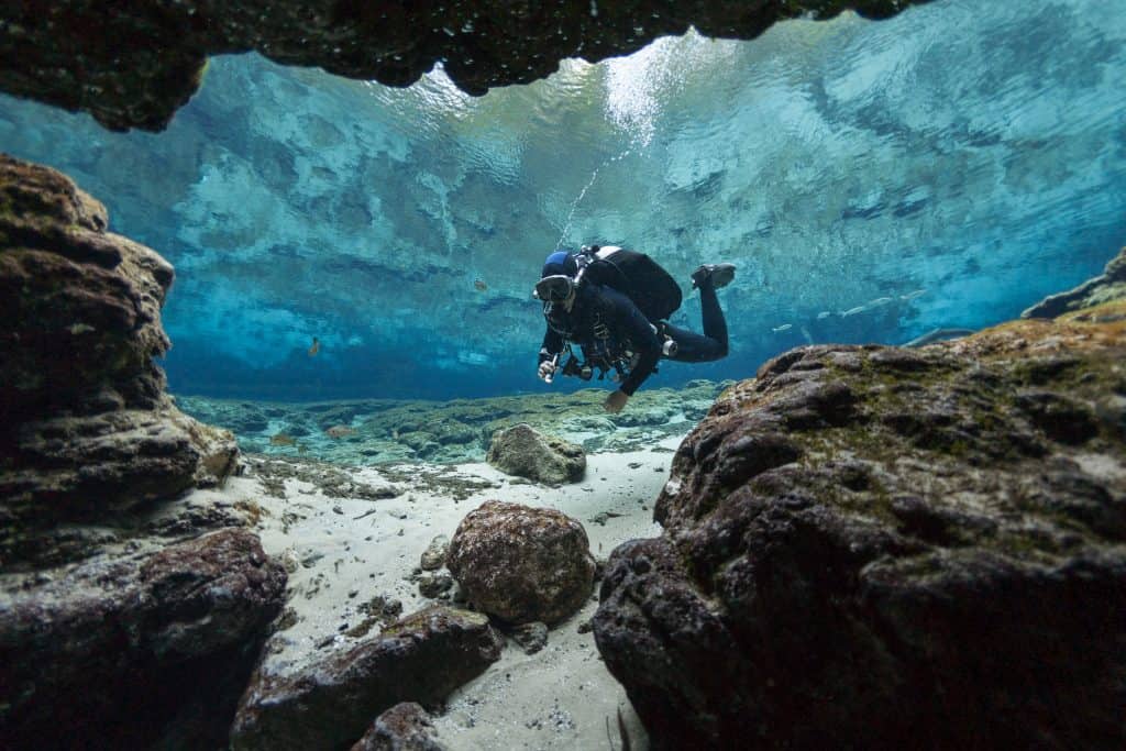 person under rocks and crystal blue water diving at ginnie springs florida