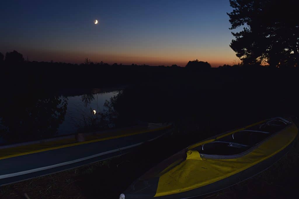 A kayak rests on the shoreline underneath the moonlight, ready for  bioluminescent kayaking in Florida.