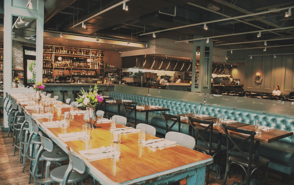 Long family style tables and booths in a rich, dark green fill the dining room at On Swann, one of the best downtown Tampa restaurants.