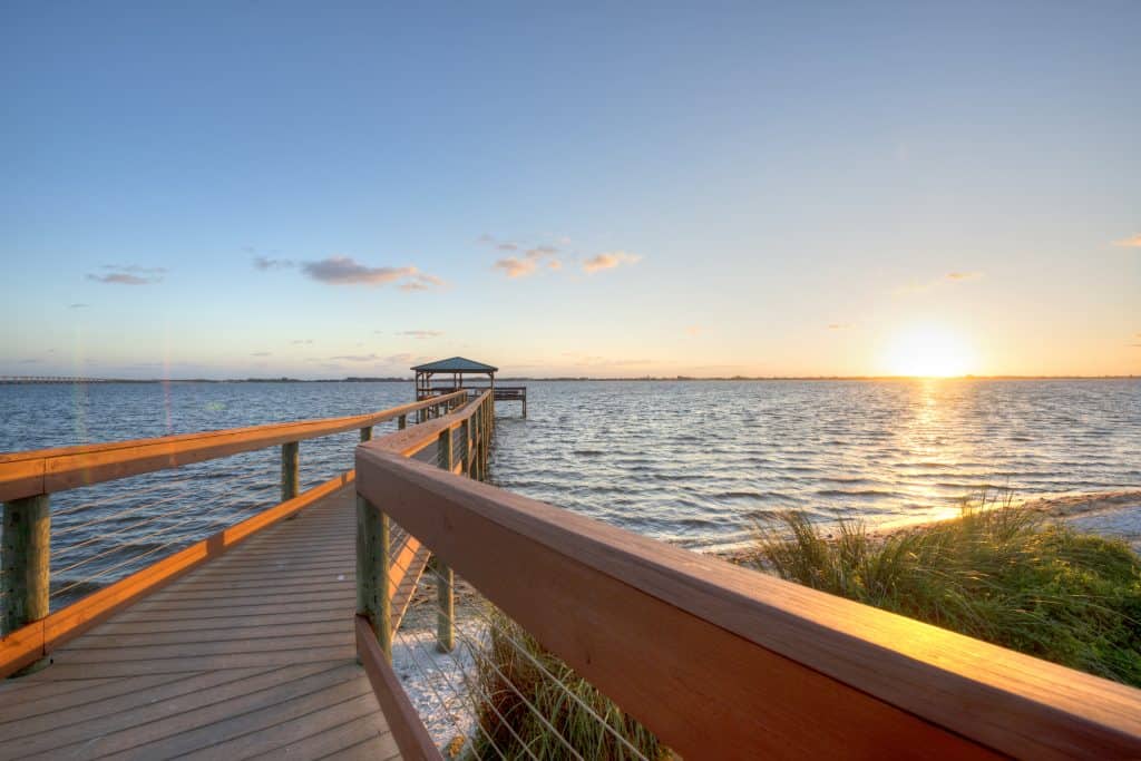 The sun sets on the waters near Melbourne Beach as seen from a dock jutting out into the ocean.