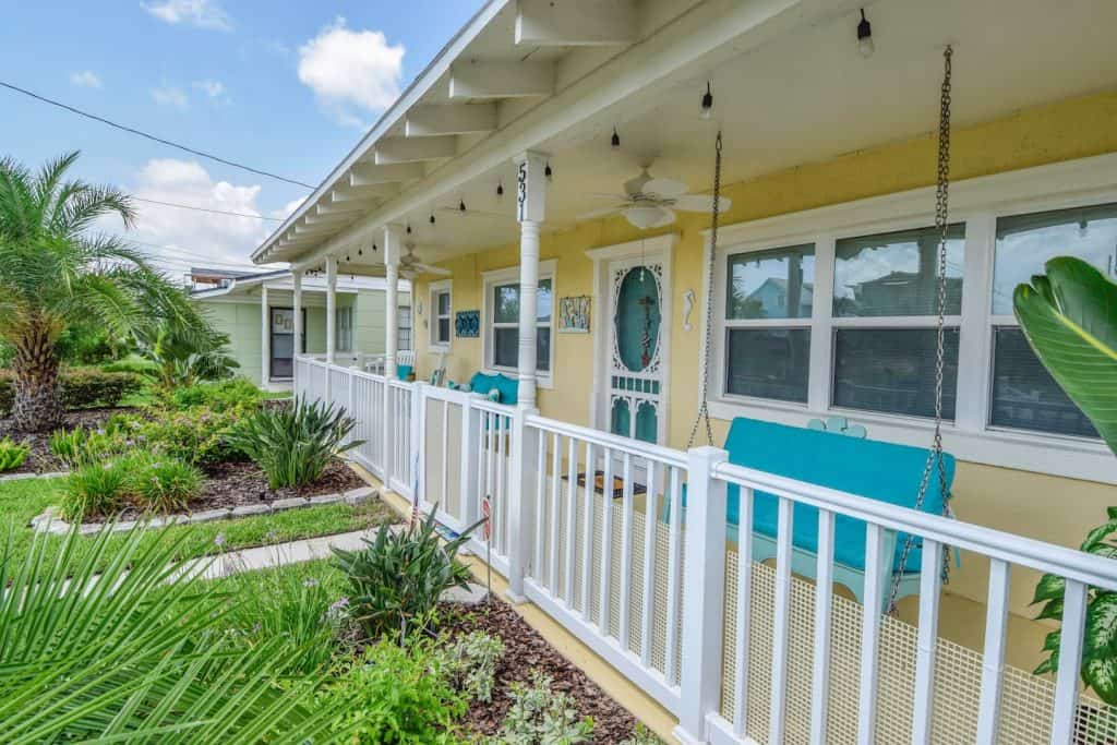 Photo of a pale yellow cottage with porch swings. 