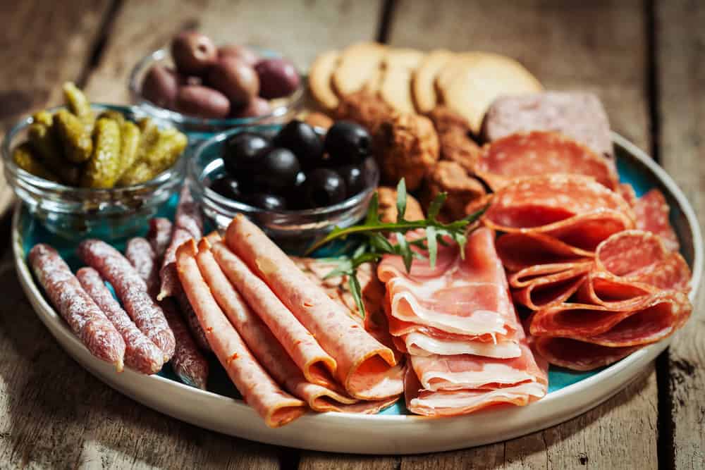 A charcuterie plate with a variety of meats, olives, and crackers.
