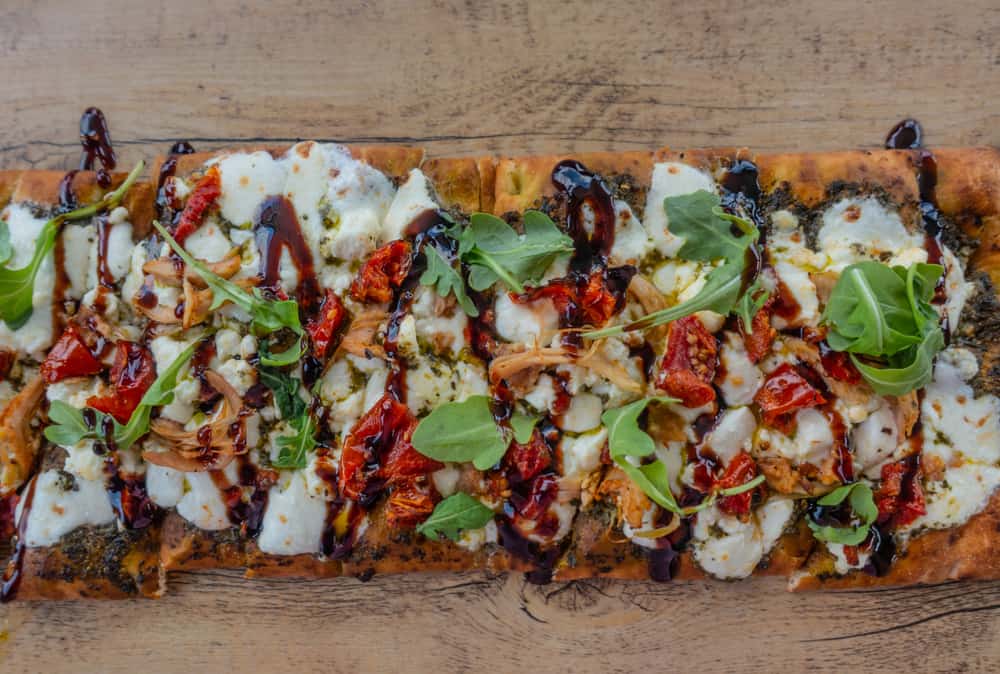 A flatbread piled with cheese, vegetables, meat, and sauce.