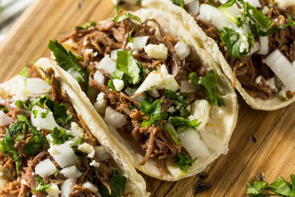 Three tacos with pock, cheese, and cilantro.