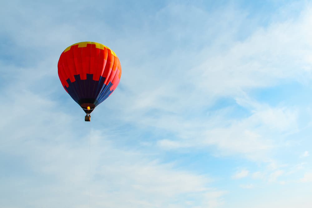 A bright, multi-colored hot air balloon floats through a light blue, partly cloudy sky. Taking a hot air balloon ride is one of the best things to do in Centra Florida.