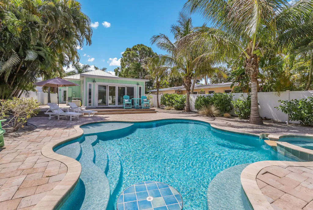 Photo of a sparkling pool with large deck behind a light green Florida cottage. 