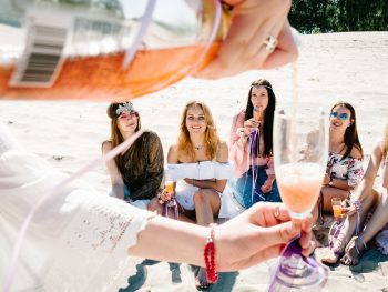 Hand pours champagne into glass in foreground with happy group of girls in background at a Florida bachelorette party