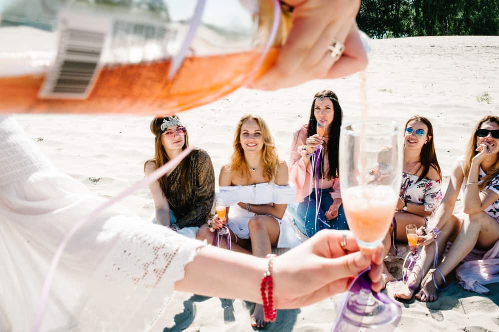 Hand pours champagne into glass in foreground with happy group of girls in background at a Florida bachelorette party