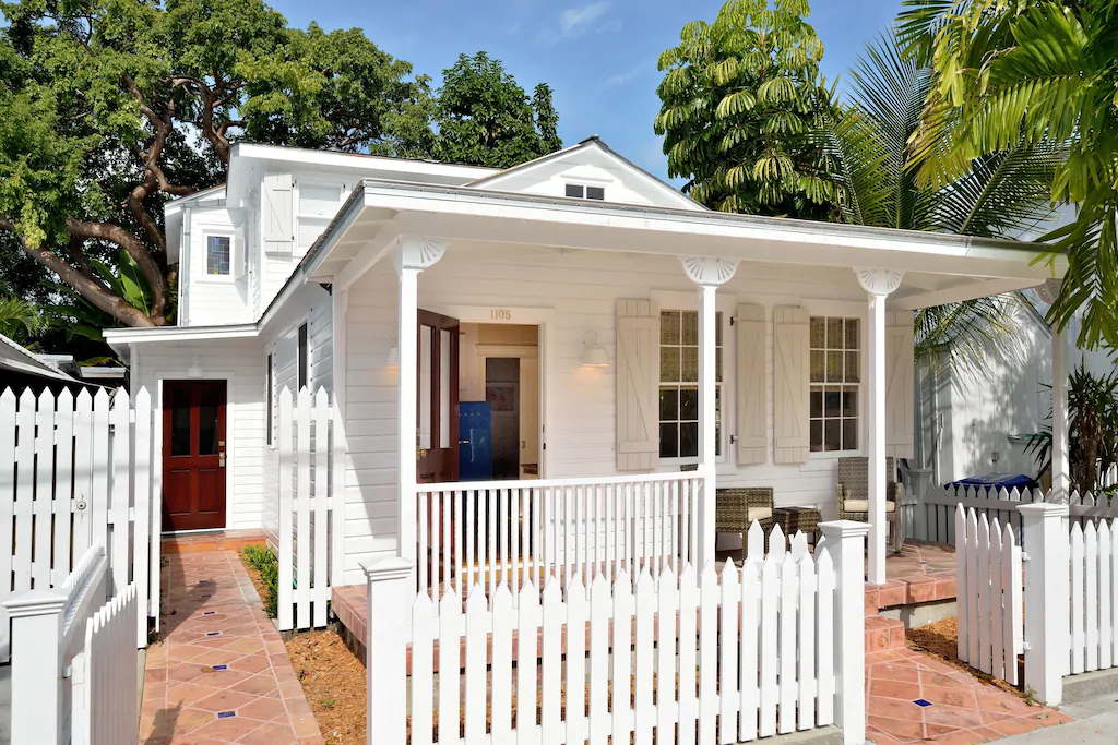 Photo of a white cottage in Florida with a white picket fence and wooden doors.