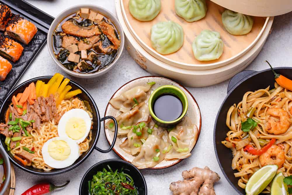 A mixture of Asian food such as dim sum, gyoza, pad thai, ramen and sushi rolls