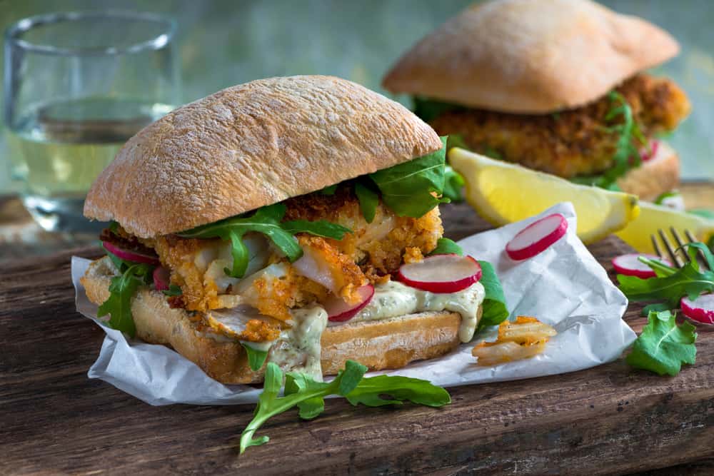 A fish sandwich with radishes, ciabatta bread and aregula on a wooden tray