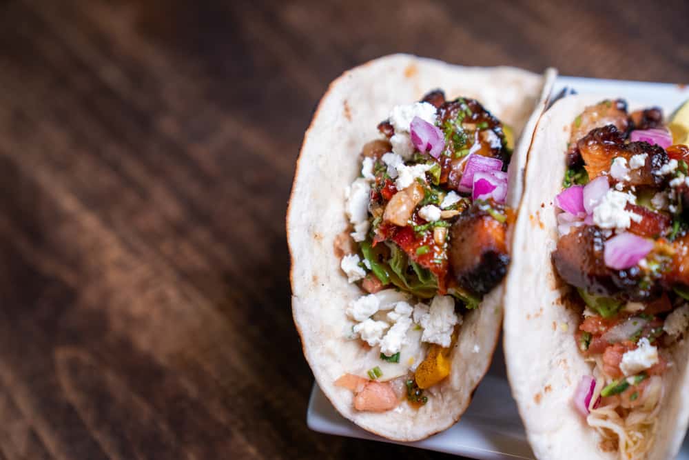 Two pork belly tacos with flour tortillas, cheese, roasted salsa with onions