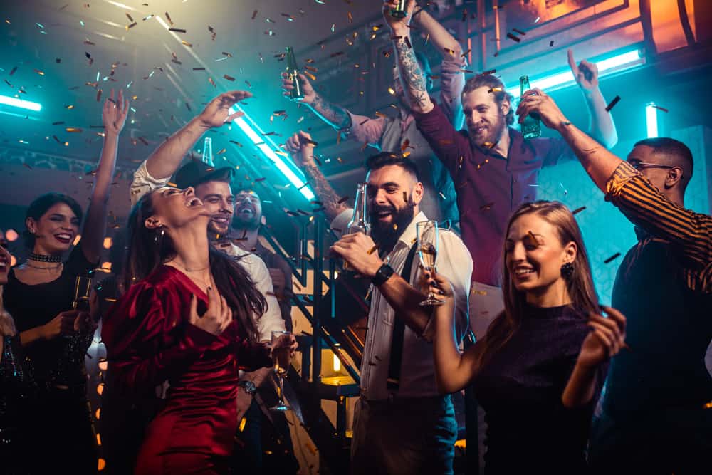 photo of adults dancing, holding champagne glasses under white lights