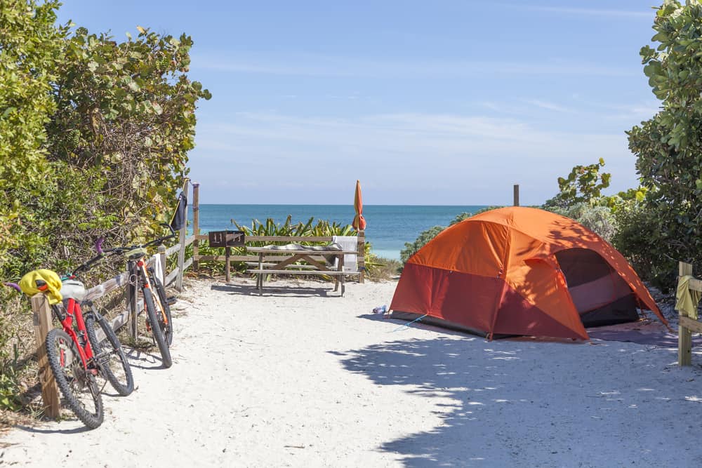 An orange tent at Bahia Honda State park with two bikes and a picnic table right on the water