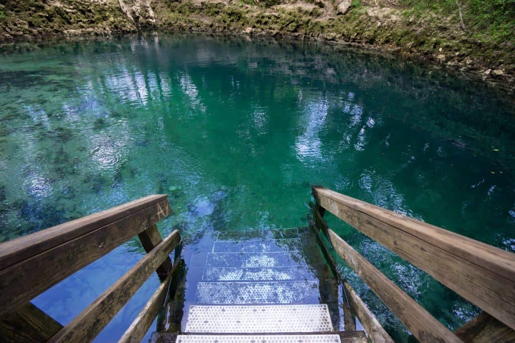 A wooden platform leads into the turquoise water at the springs with limestone walls.