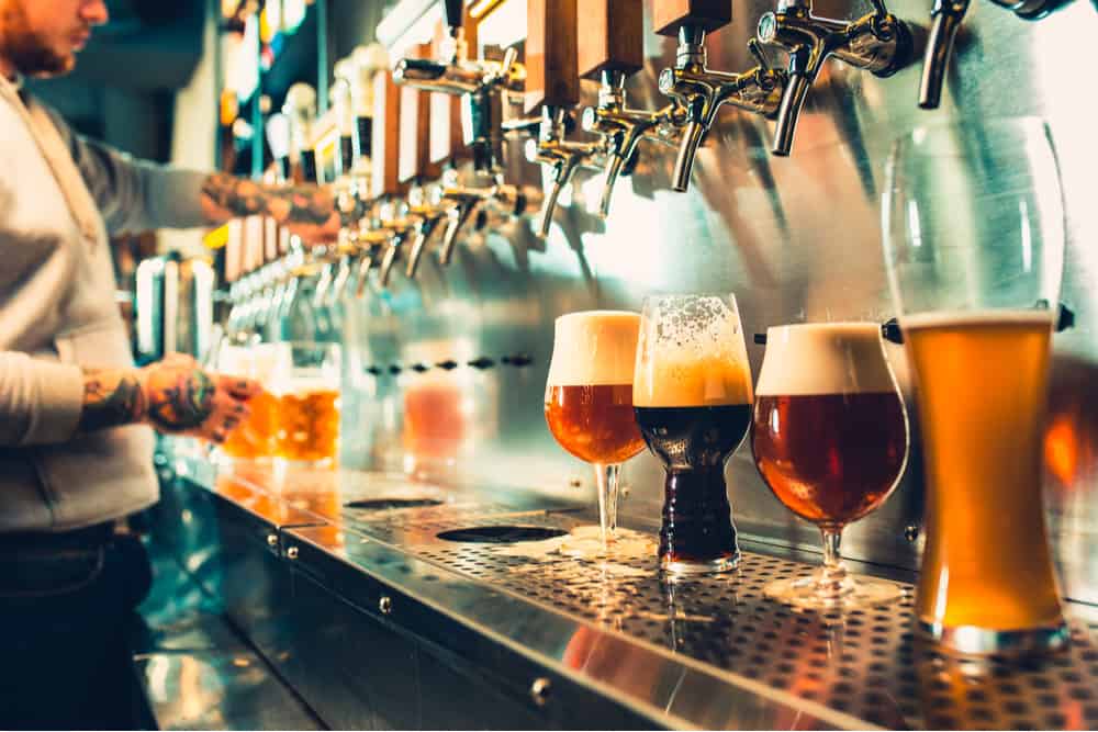 A large variety of beers on tap poured into tall glasses
