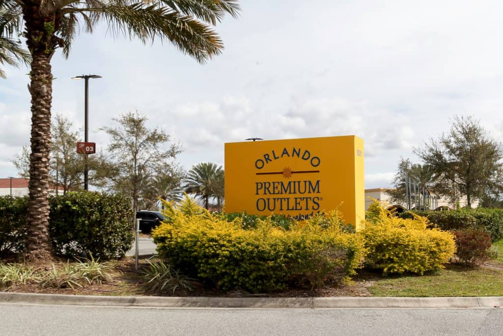 The yellow Orlando Premium Outlets sign under a palm tree.