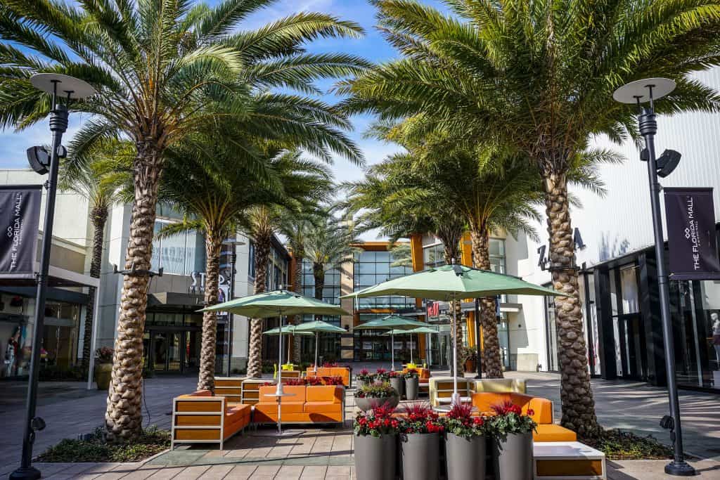 An empty, outdoor shopping section with seating areas and palm trees.