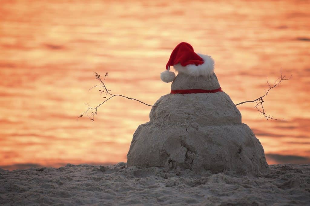 A snowman made out of sand with a Santa hat at sunset on a beach