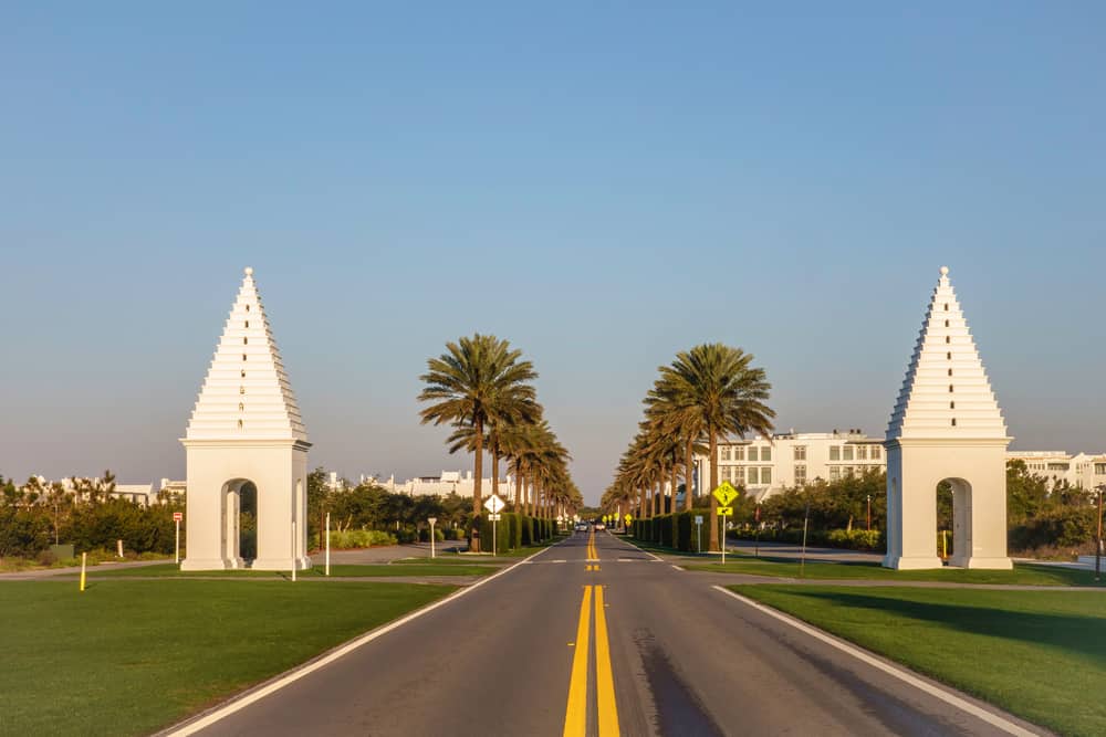 The road of Highway 30A in Florida, with palm trees and steepled structures on both of the road.