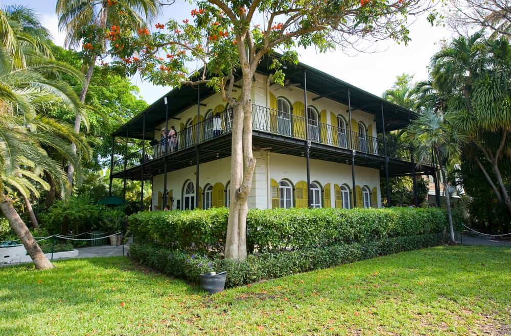 The Hemingway house is two stories, yellow, and features historic architecture. 