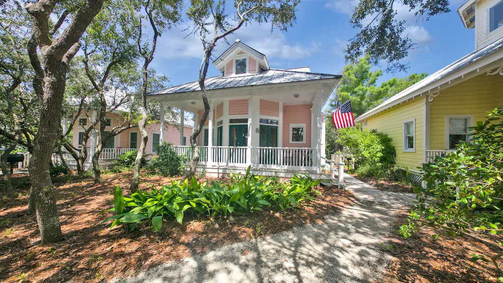 A pink beach house with an American flag and a beautiful front garden.