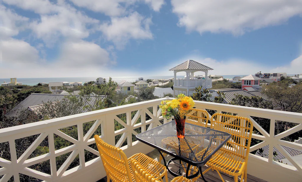 Two yellow chairs and a table on a balcony looking out at the view over Seaside.