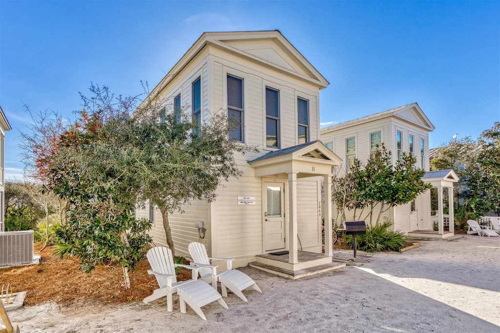 A white rental house with a tree and chairs outside