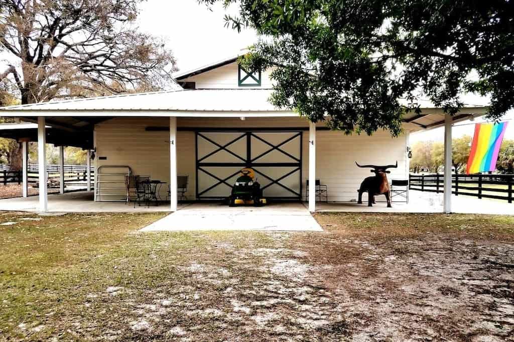 External view of the barn, a sculpture of a bull, a John Deere riding mower, and an LGBTQ+ flag are visible outside the barn. 