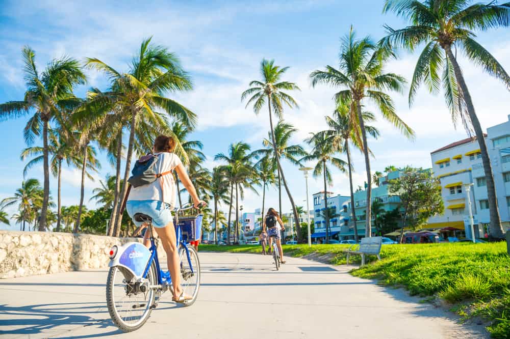 cyclists on a path with palm trees and buildings on one of the bike trails in florida