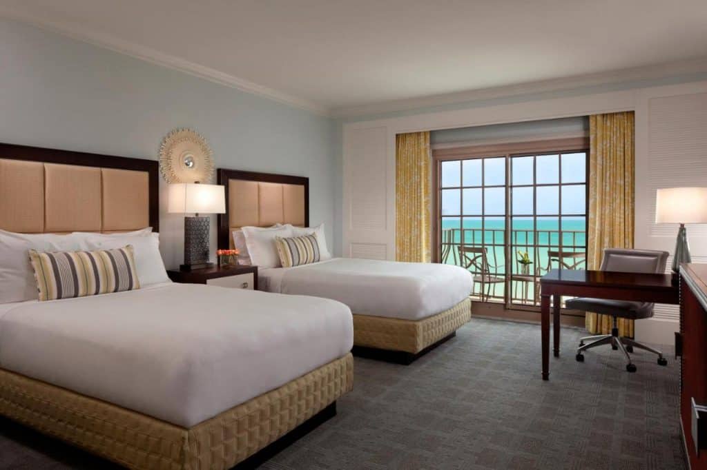 The interior view of the Ritz-Carlton in Naples that overlooks blue waters from the balcony and features two beds in the room.