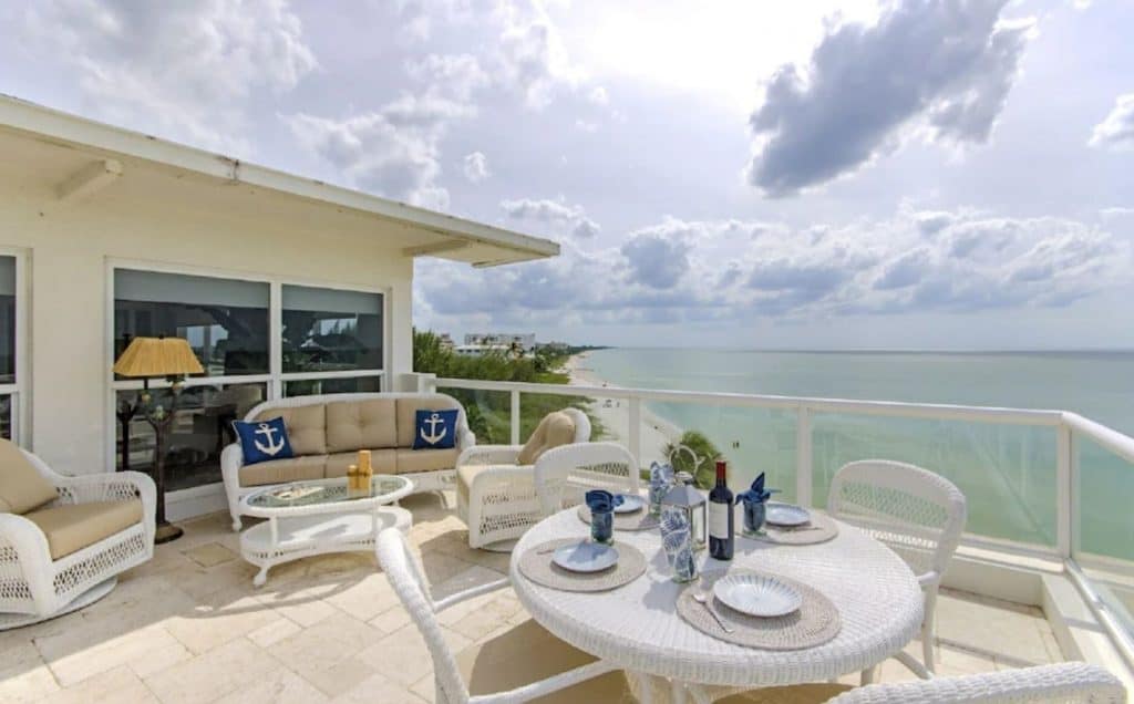 A balcony attached to a 7th floor penthouse. There is whicker seating on the balcony and you can see the gulf of Mexico and the shoreline. 