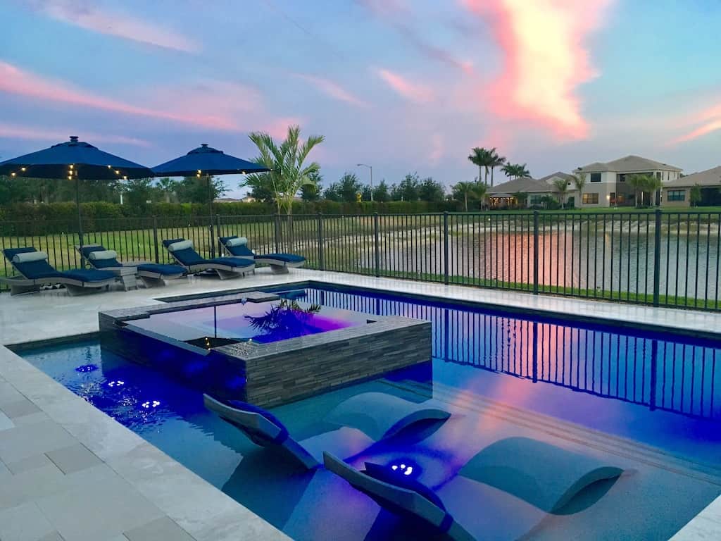 Sunset over the Executive Waterfront Homes private pool featuring partially submerged luxurious lawn chairs. 