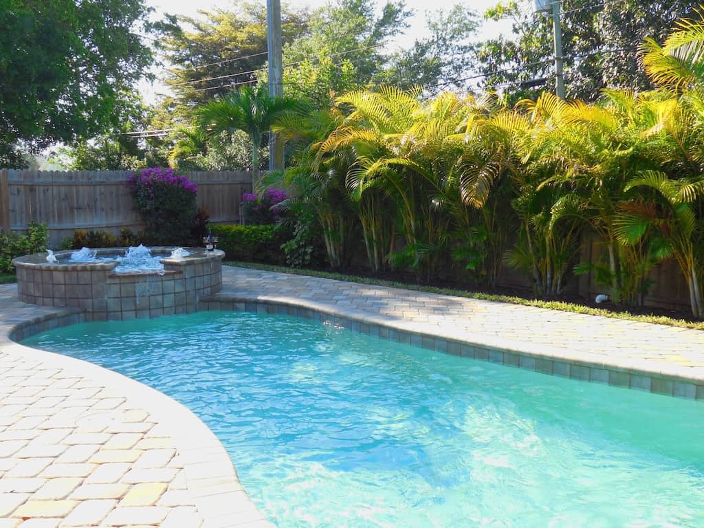 View of the pool, spa, palms, and bougainvillea of the backyard of the Walk to Beach property, one of the best VRBO's in Naples. 