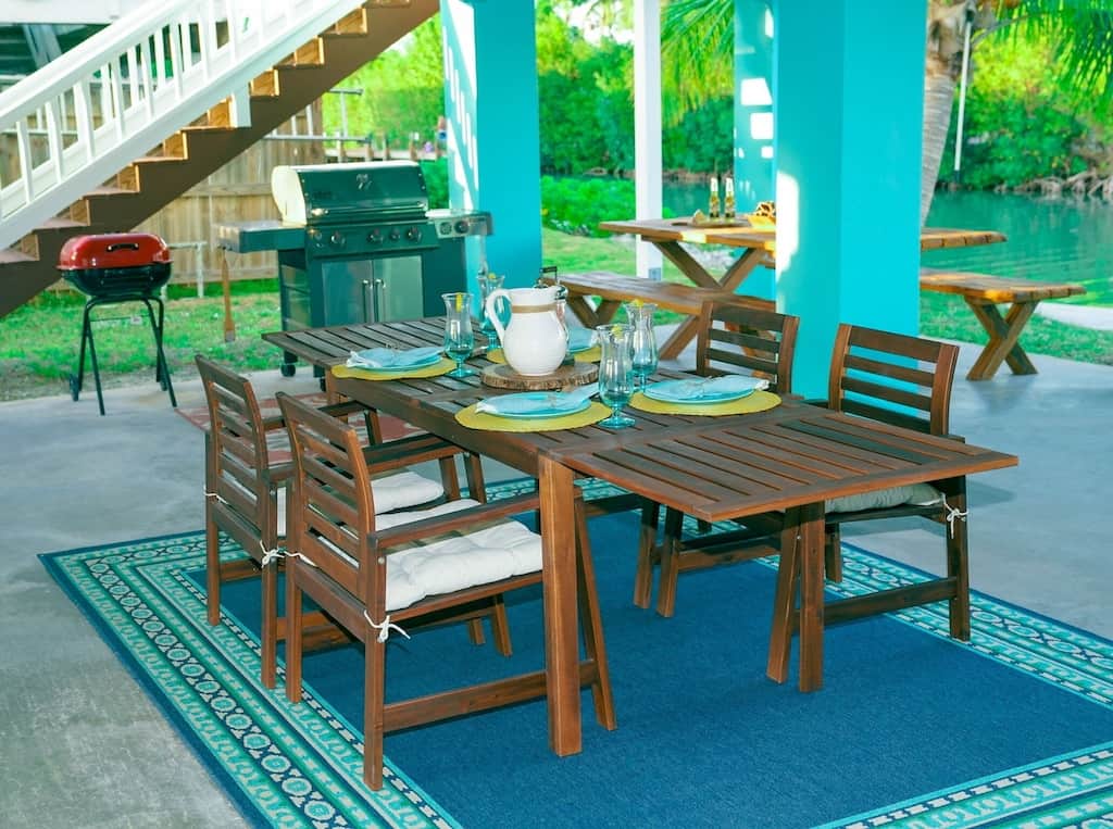 A view of an luxurious teal themed outdoor patio with plenty of seating and a two outdoor grills. The teal blue canal is visible in the background. 