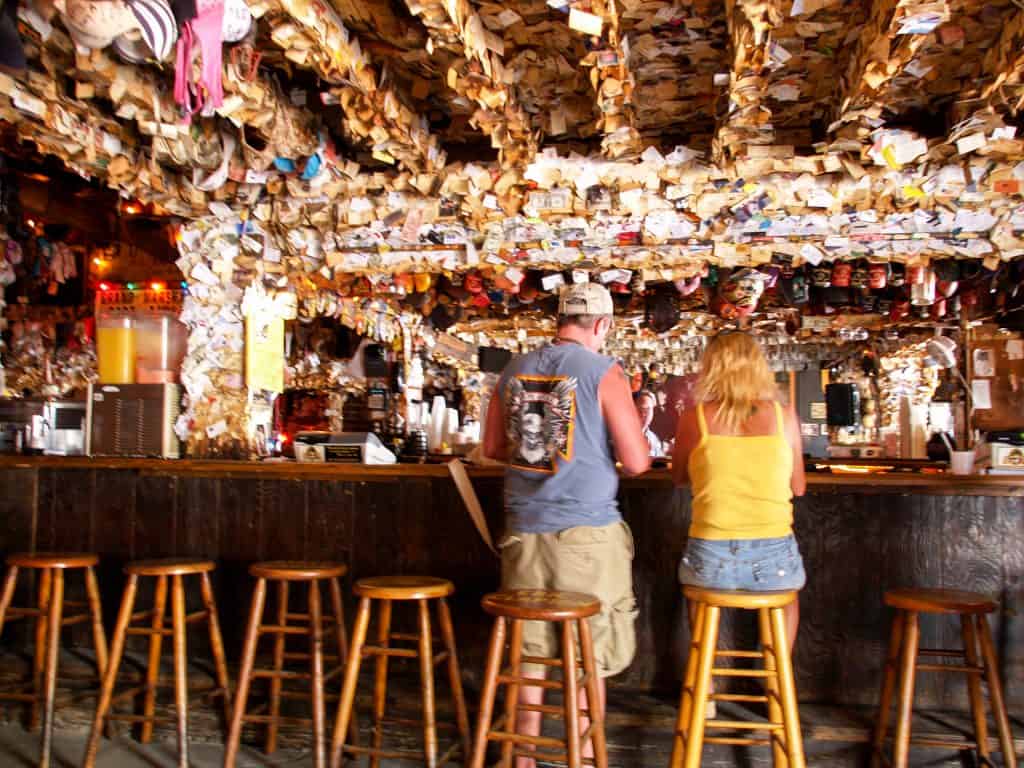 A shot of the inside of a bar that has walls and ceiling covered in drawings and postcards and coasters from the customers, giving a very unique atmosphere