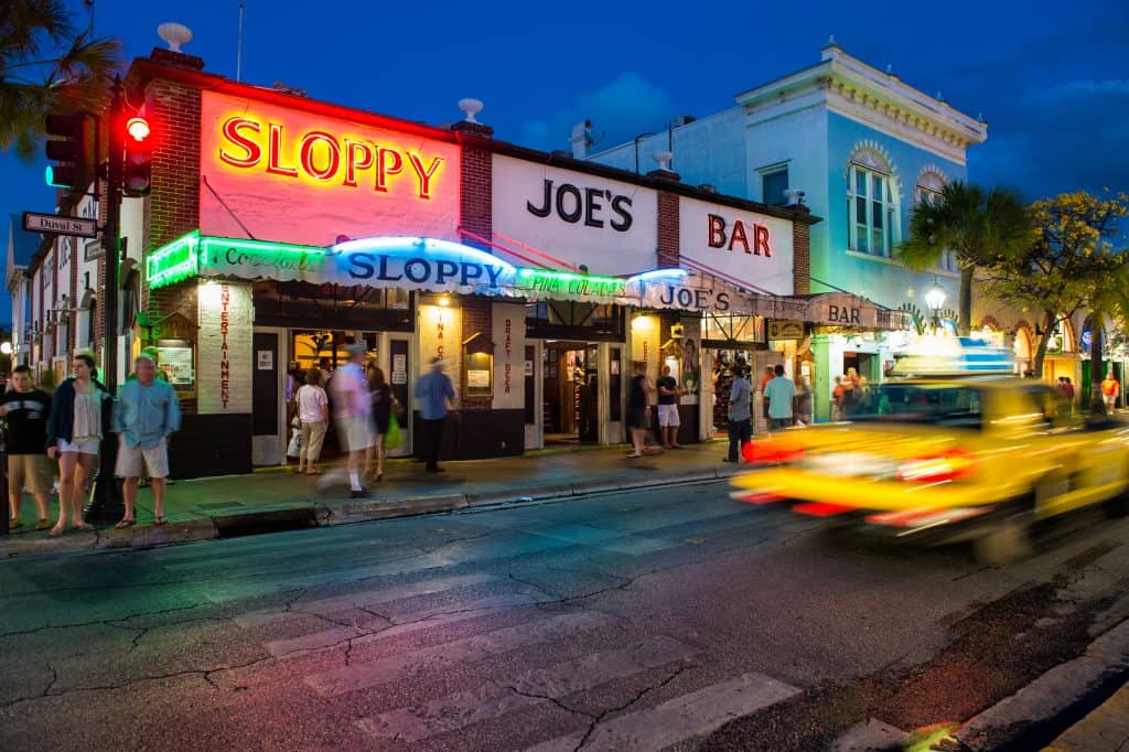 A nighttime shot of a busy intersection on duval street featuring the bar' sloppy joe's' and the colorful lights adorning the front entrance