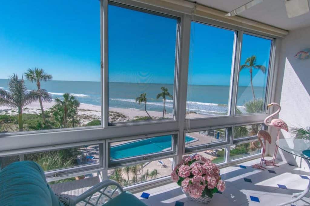 The sunroom of a private condo on the beach in Naples Florida. You can see a large pool, the beach with palm trees, and the 80's style decor of the sunroom. 