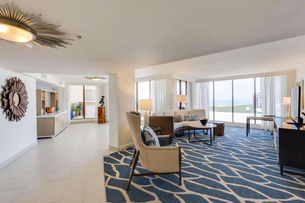 The interior of a suite in one of the hotels on the beach in Naples Florida. It has a large sitting area, a private balcony with views of the gulf, and is decorated in a very modern style. 